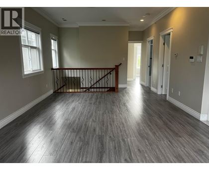 A spacious room with a wooden floor and a staircase with a metal railing.