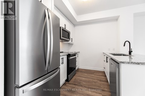 A kitchen with a stainless steel refrigerator and a microwave above the oven.