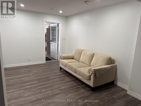 A beige couch sits in a room with white walls and wood flooring.