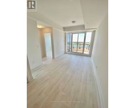 A spacious room with wooden flooring and a view of the beach through the windows.