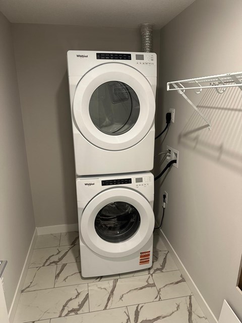 A white dryer and washer are stacked on top of each other in a small laundry room.