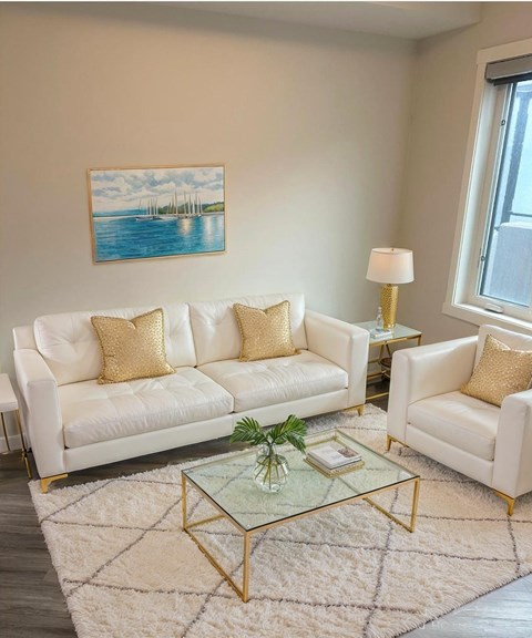 A living room with a white sofa, a glass coffee table, and a painting on the wall.