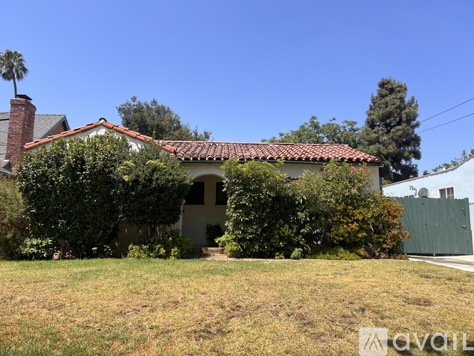 A house with a red tile roof is surrounded by greenery.