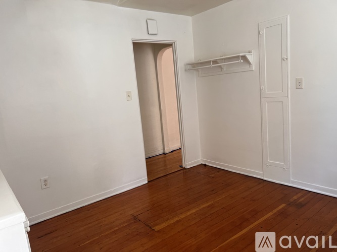 A room with a wooden floor and white walls, with a door and a shelf.