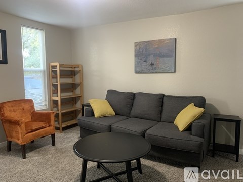 A living room with a grey couch, a brown chair, a black table, and a painting on the wall.