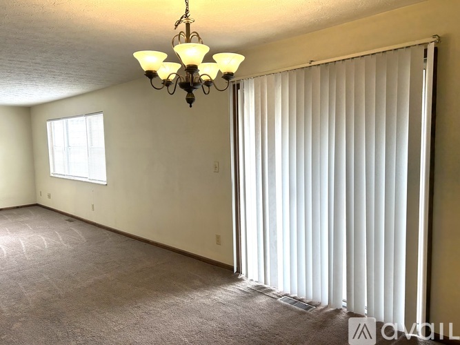 A room with a chandelier, carpeted floor, and a window with blinds.