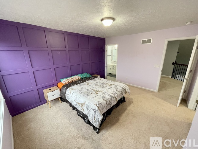 A bedroom with purple walls and a bed with a white and patterned bedspread.