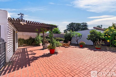 A patio with a white building and a tree in the background.