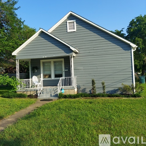 A small house with a grey siding and a white porch.