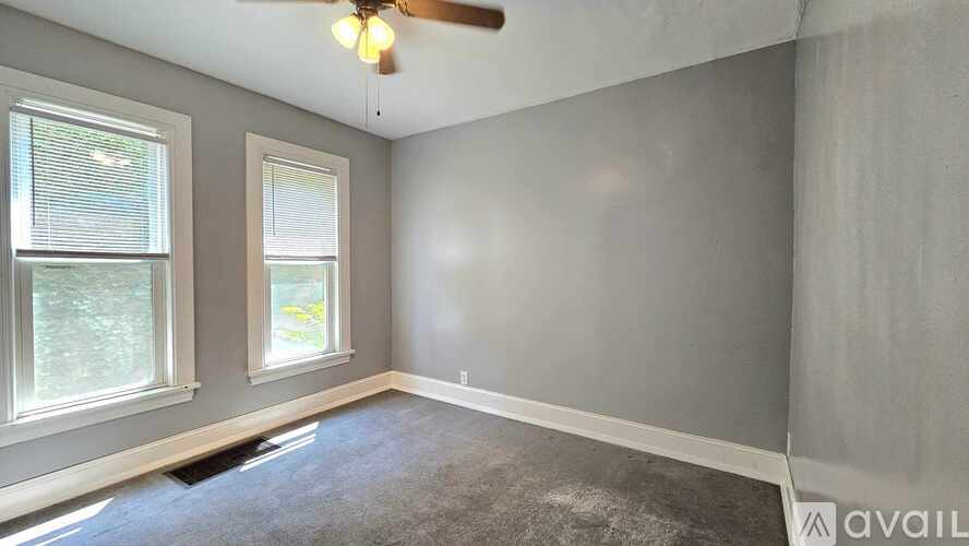 A room with a ceiling fan and two windows.