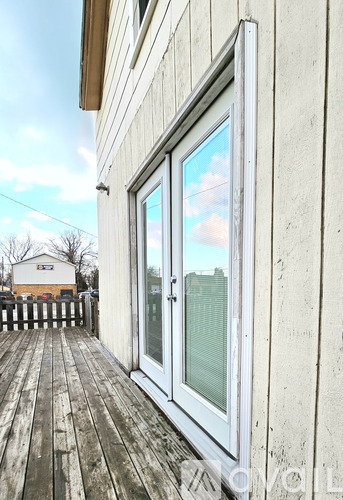 A white door with a window is on a wooden deck.