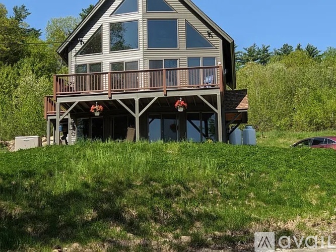 A house with a balcony and a deck is surrounded by greenery.
