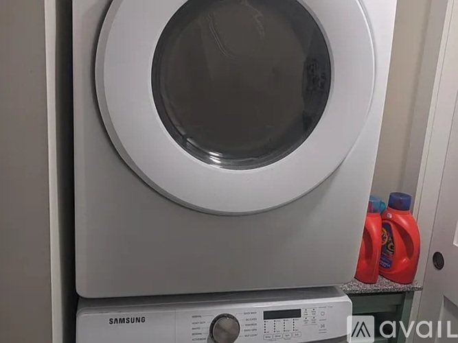 A Samsung washing machine with the door open and a bottle of detergent on top.