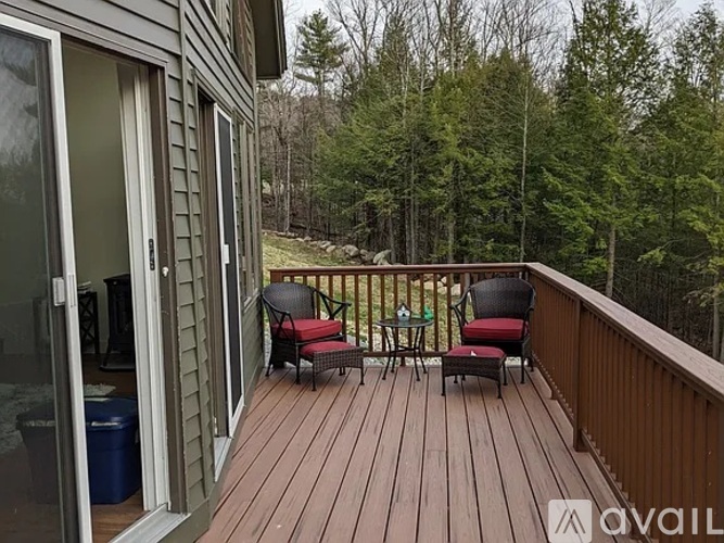 A deck with two chairs and a table is surrounded by trees.