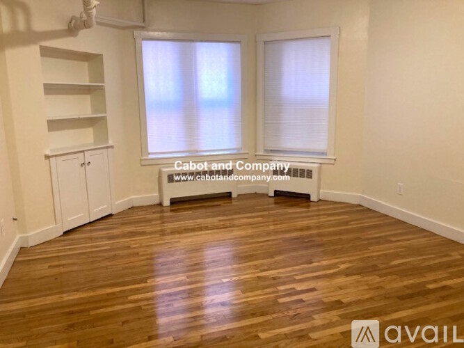 A room with wooden flooring and two windows, one of which has blinds.