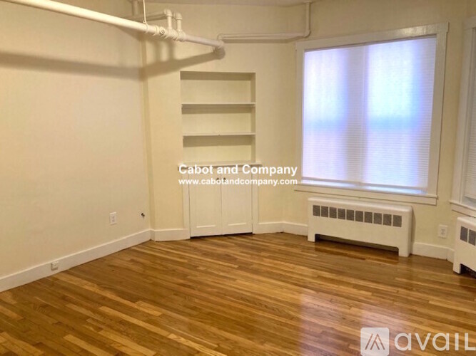 A room with wooden floors and white walls, with a window and a bench.