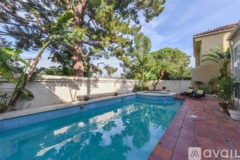 A pool surrounded by trees and a patio with chairs.