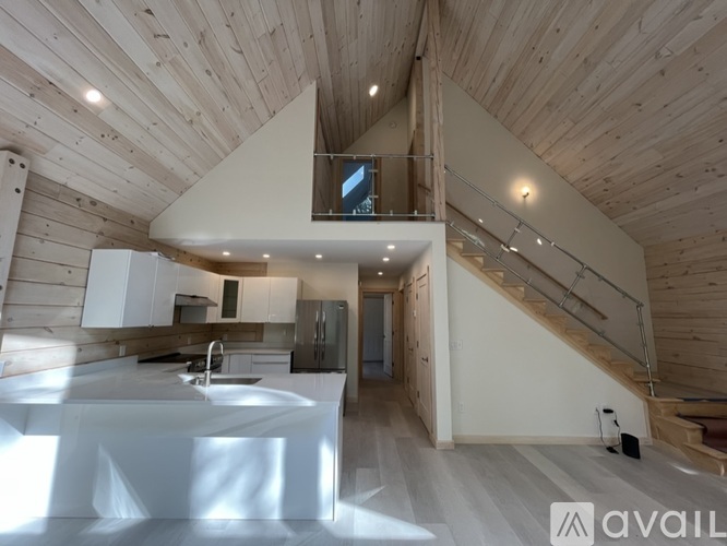 A modern kitchen with a wooden ceiling and a staircase leading to the upper floor.