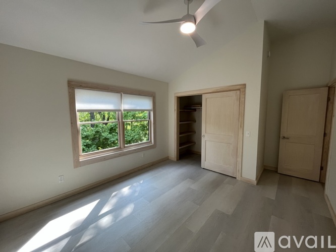 A room with a ceiling fan and a window overlooking a green area.