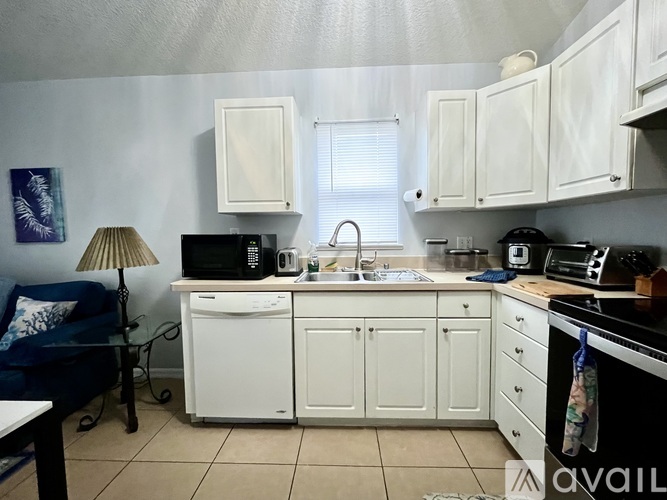 A kitchen with white cabinets and appliances, a blue couch, and a painting on the wall.