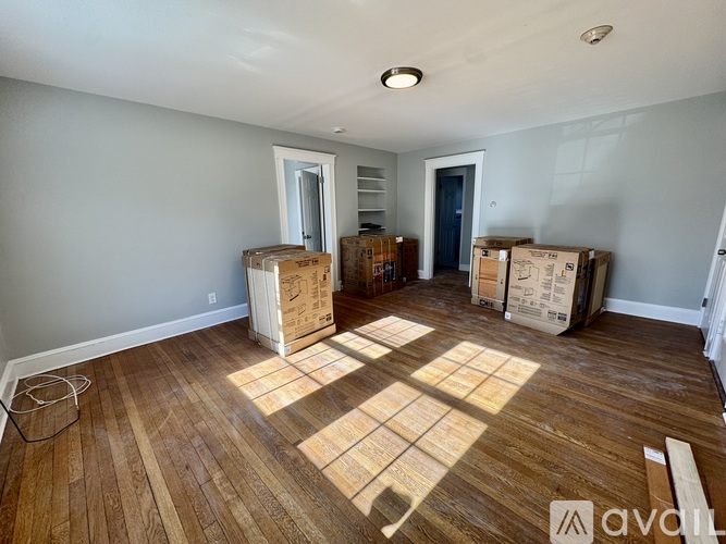 A room with wooden flooring and cardboard boxes scattered around.