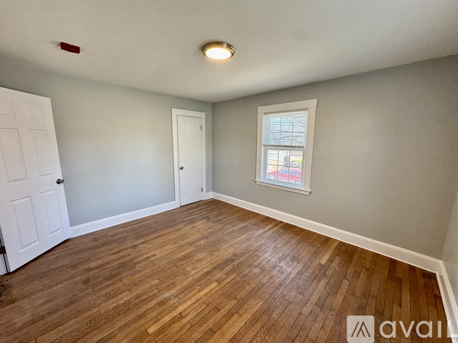 A room with wooden flooring and a window showing a red building outside.