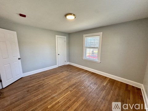 A room with wooden flooring and a window showing a red building outside.