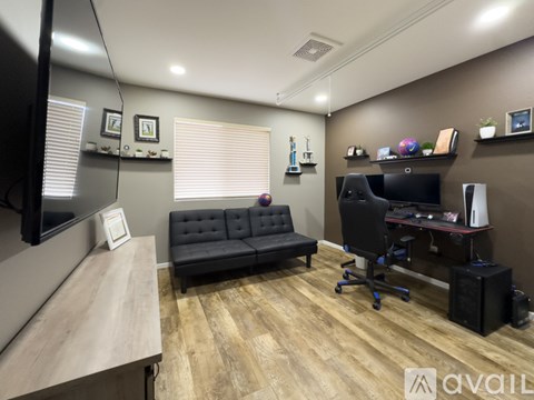 A modern office space with a black couch, a desk with a computer, and a TV on the wall.