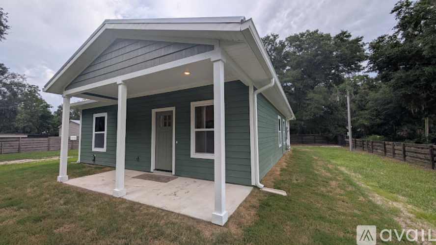 A small green house with a porch and a fence in the background.