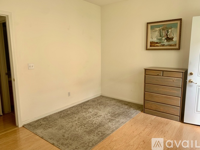A room with a rug, a wooden dresser and a painting on the wall.