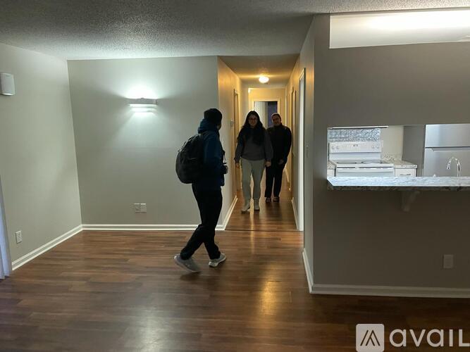 Three people walking through a room with wooden floors and white walls.