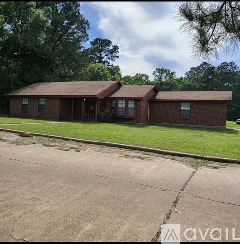 A house with a brown roof and a porch is surrounded by green grass and trees.