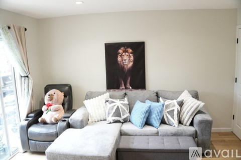 A living room with a grey couch, a chair, and a painting of a lion on the wall.