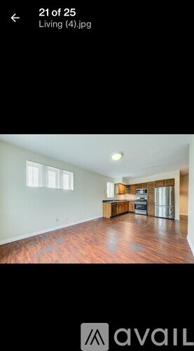 A living room with a wooden floor and a kitchen area in the background.