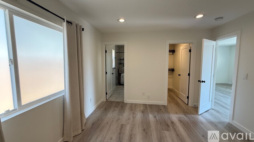 A spacious room with wooden flooring and a large window on the left side.
