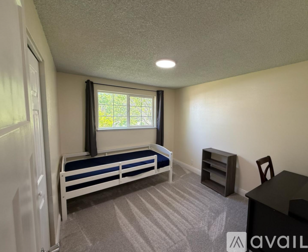 A bedroom with a bed, desk, and window.
