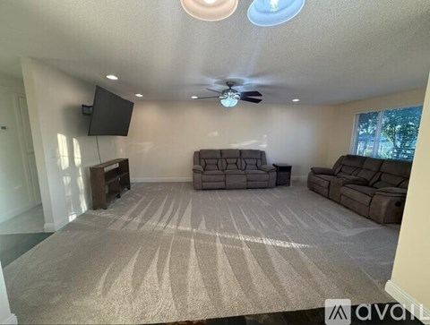 A living room with a grey carpet and a brown couch.