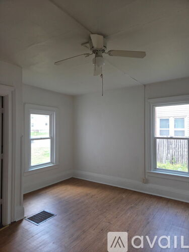 A room with a ceiling fan and two windows.