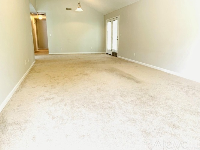 A spacious room with beige carpeting and white walls.