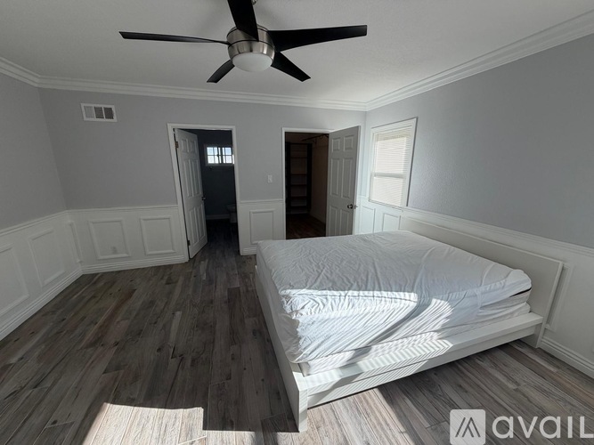 A bedroom with a bed, a ceiling fan, and a wooden floor.