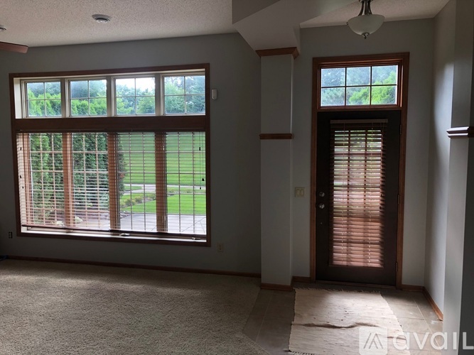 A room with a carpeted floor and a view of a green lawn through a window.