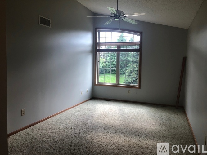 A room with a carpeted floor, a ceiling fan, and a window with a view of trees.