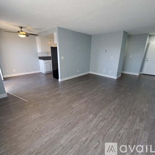 A room with a ceiling fan and light, a kitchenette, and a doorway leading to another room.