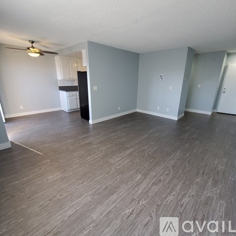 A room with a ceiling fan and light, a kitchenette, and a doorway leading to another room.