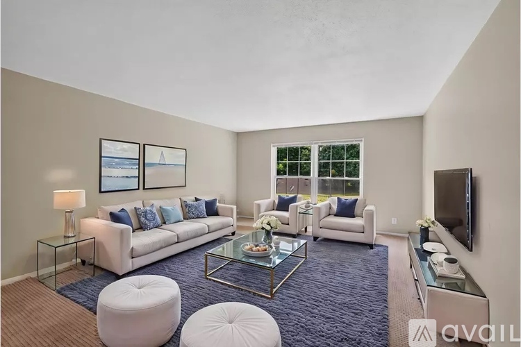 A living room with a white couch, a glass coffee table, and a television.