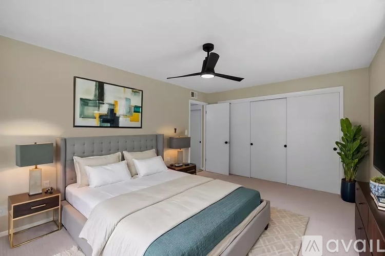 A bedroom with a large bed, a ceiling fan, and a painting on the wall.