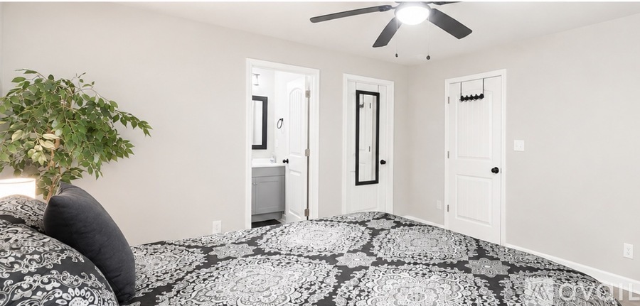 A bedroom with a black and white patterned bedspread and a ceiling fan.