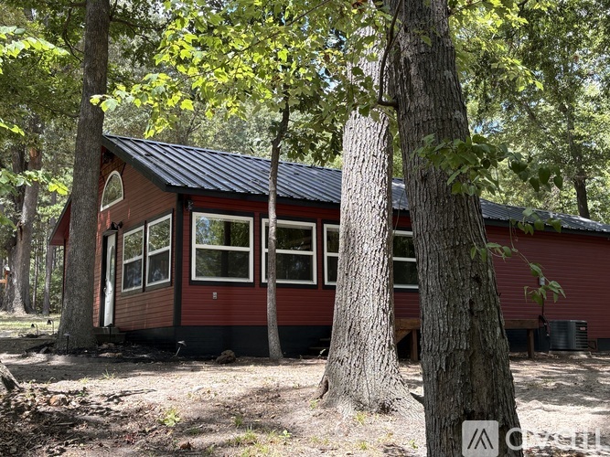 A red house with a black roof is surrounded by trees.