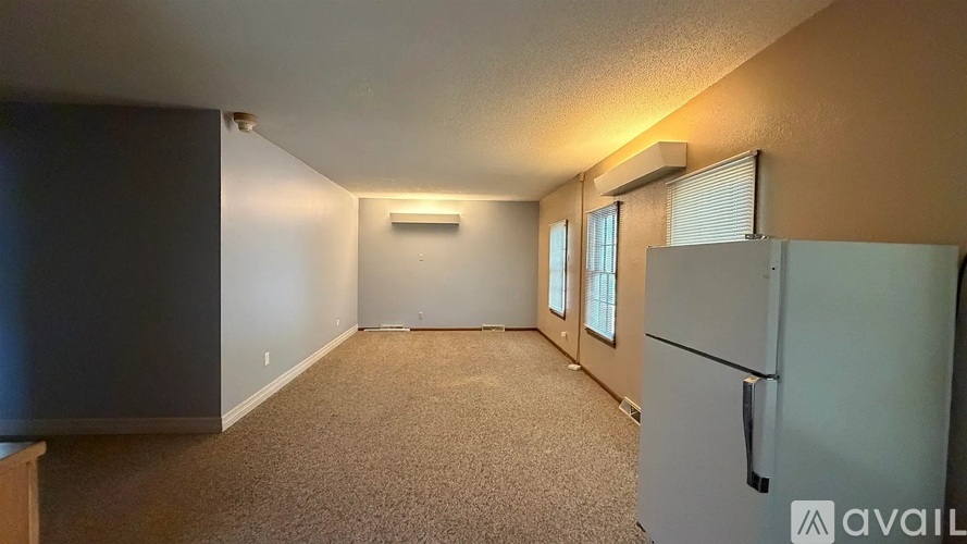 A spacious room with a carpeted floor and a white refrigerator.