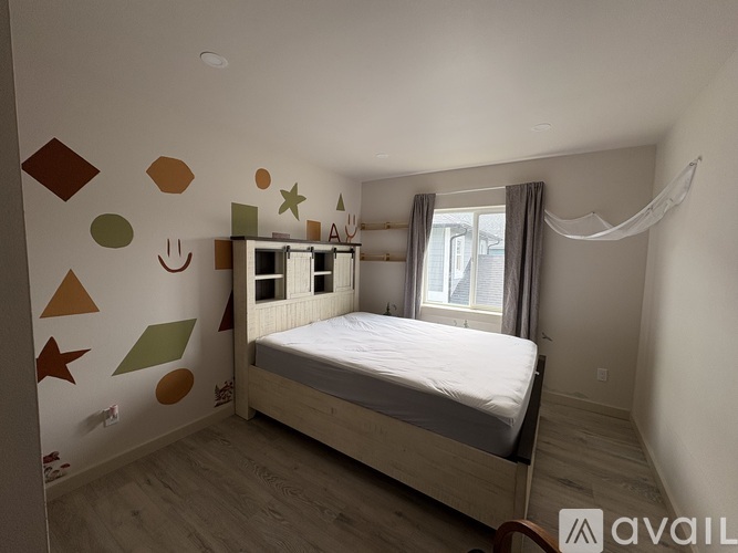A bedroom with a bed, a window with curtains, and a wall with various shapes drawn on it.